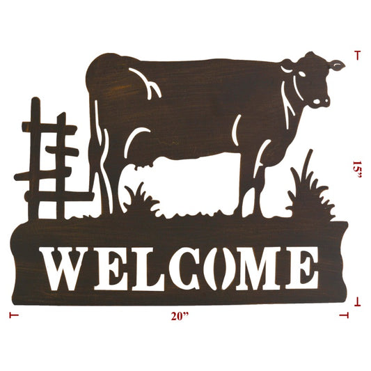 Metal cow welcome sign with cow standing on grass next to a fence
